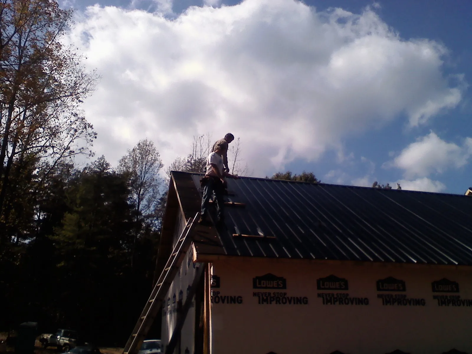 Roofer fastening dark metal panels high against a cloudy sky, from a Roof Inspection job in Pembroke