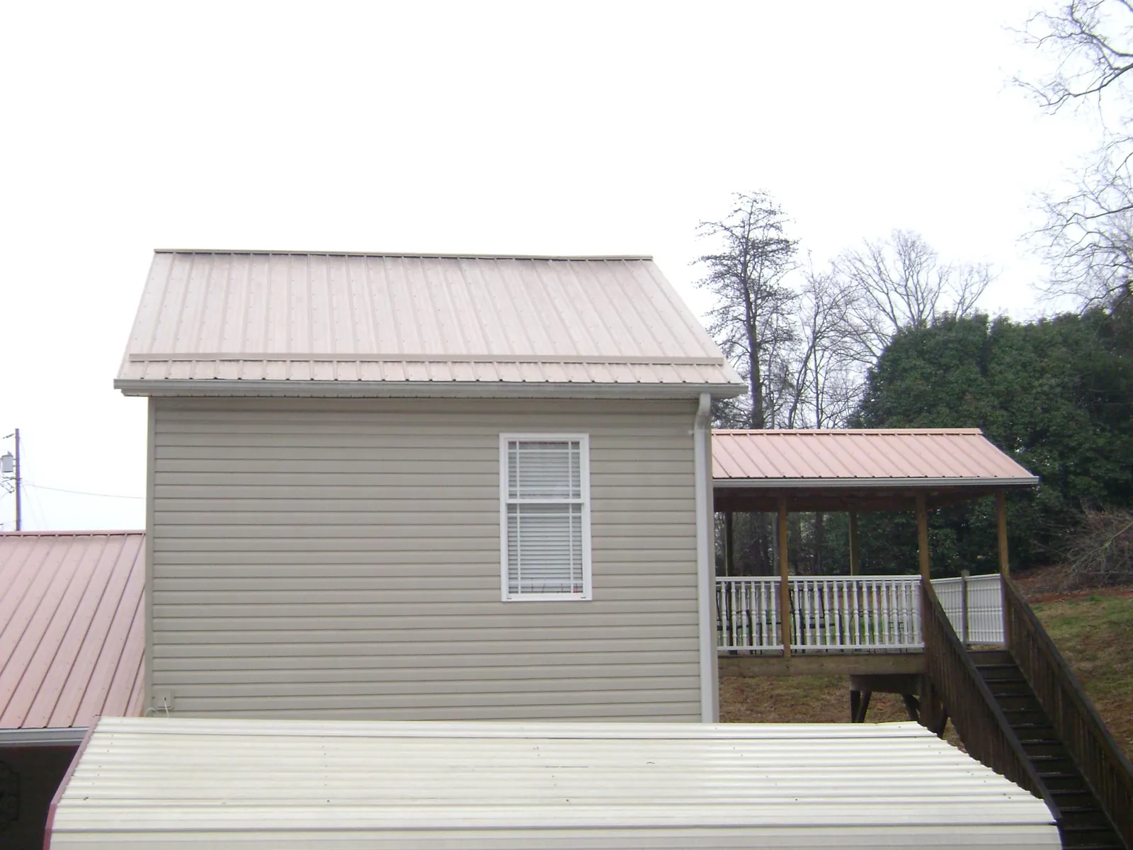 Tan metal roofs on a two story addition and attached porch, from a Roof Replacement job in Pembroke